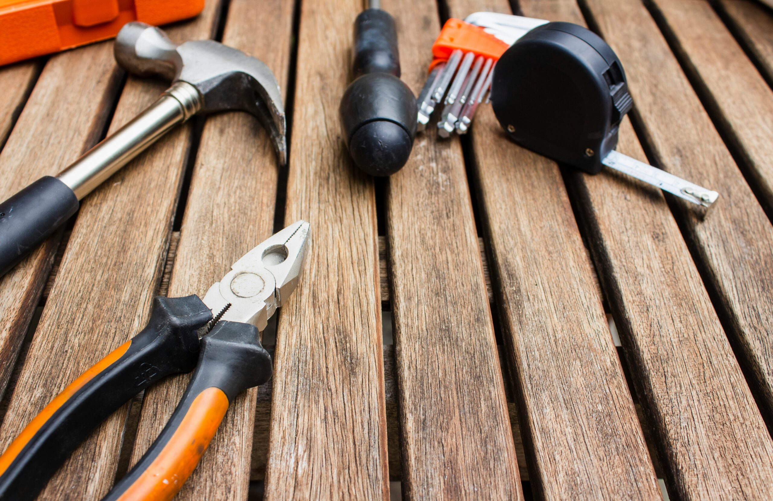 Basic hand tools including hammer, pliers, hex keys, and tape measure on wooden table